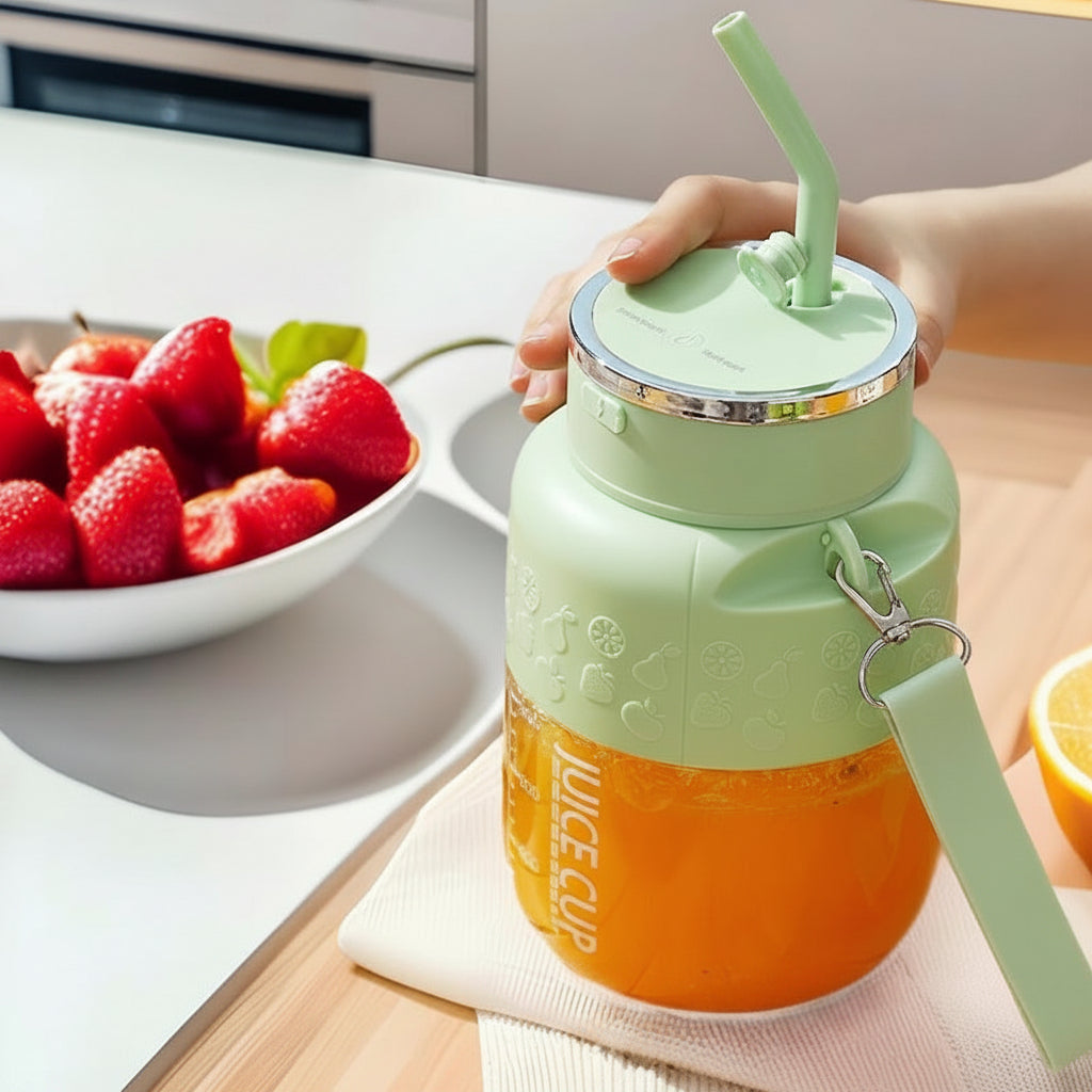 Green juice cup with straw and orange juice, next to a bowl of strawberries on a table.