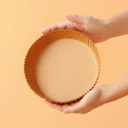 Hand holding a round baking mold against an orange background.