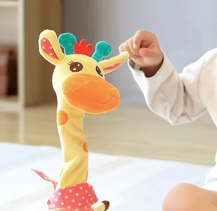 A baby's hand gently touches a yellow dancing talking giraffe toy with colorful accents, including teal and red spots on the ears and a pink polka-dot skirt, in a softly lit indoor setting.